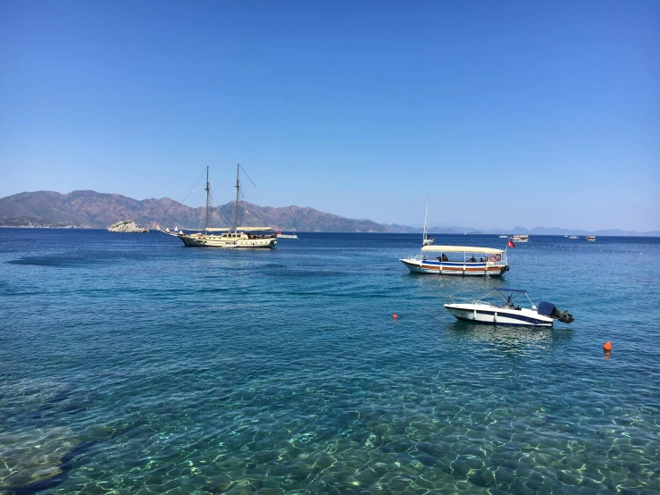 several boats in the ocean with mountains in the background