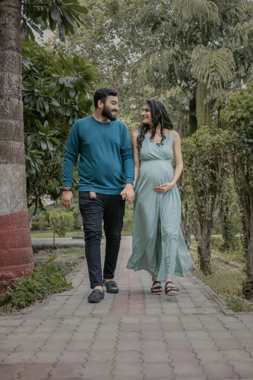 pregnant couple walking along path through trees holding hands