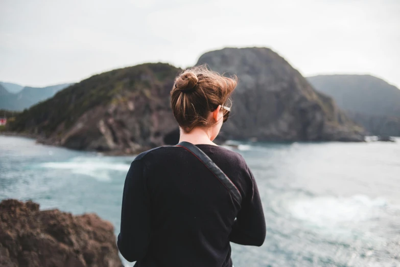 a woman that is sitting on a rock overlooking the ocean