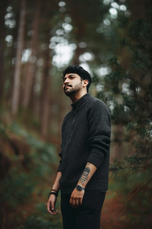 the man is posing in the woods with his hands on his hips