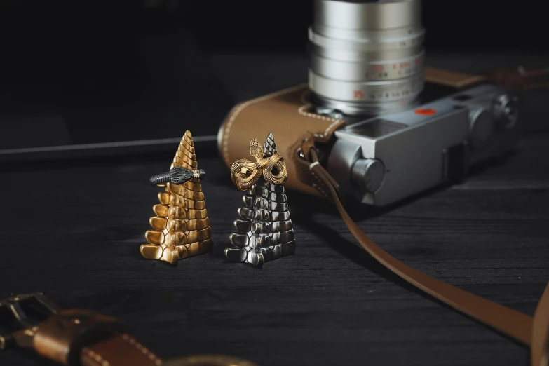 two golden charms sit next to a camera