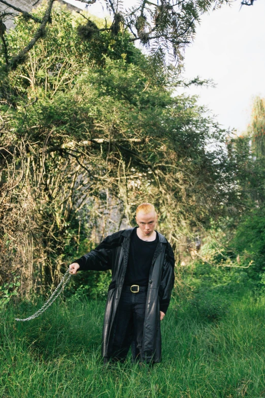 a man standing on a grassy field wearing a black coat