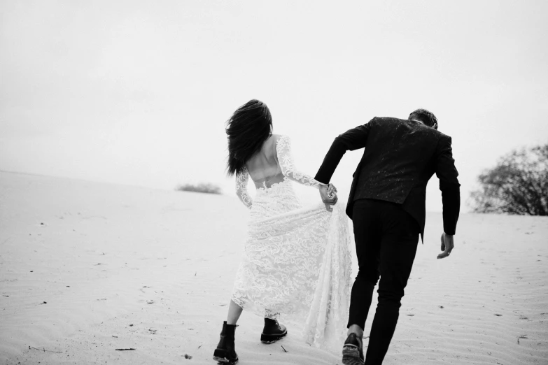 black and white po of a bride and groom running through the sand