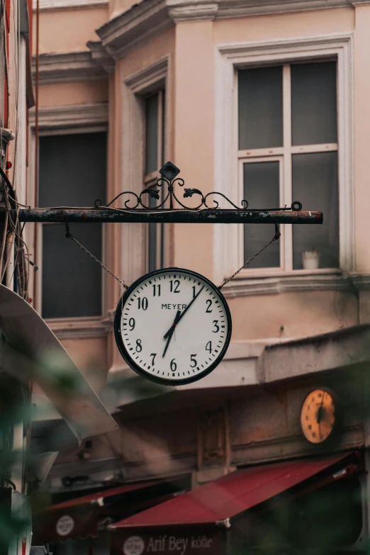 a white clock hanging on a metal pole near a building