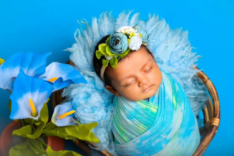 a newborn baby wrapped in blue with flower hairband