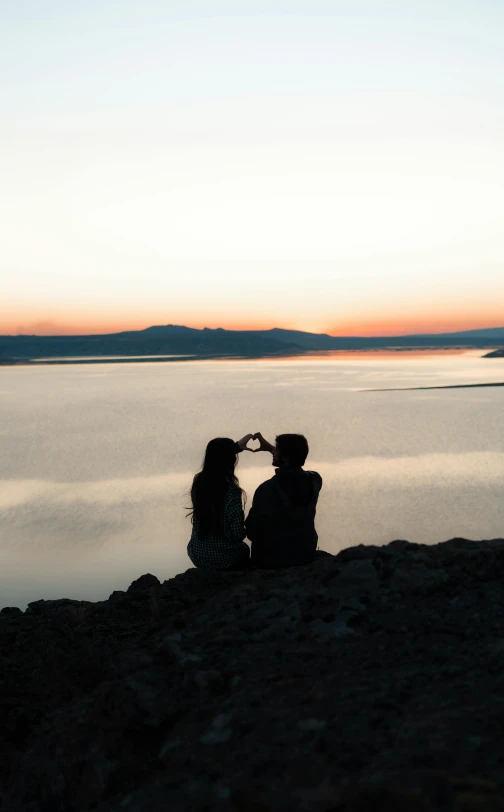 two people sitting by the water with their hands in each other's mouths