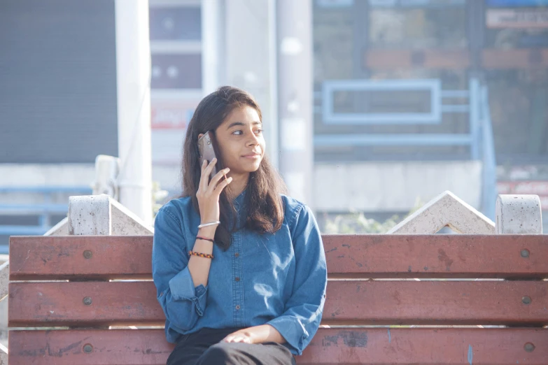 a woman is sitting on a bench talking on her phone