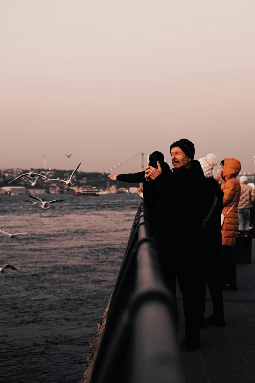 three people stand on the pier looking out at seagulls