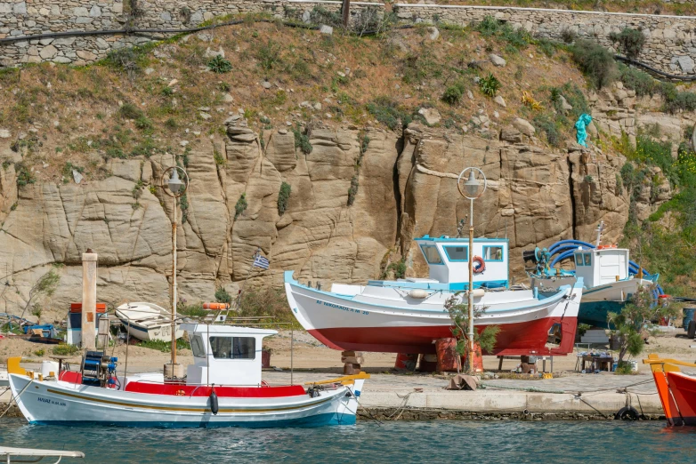 two boats in the water sitting near a stone mountain side