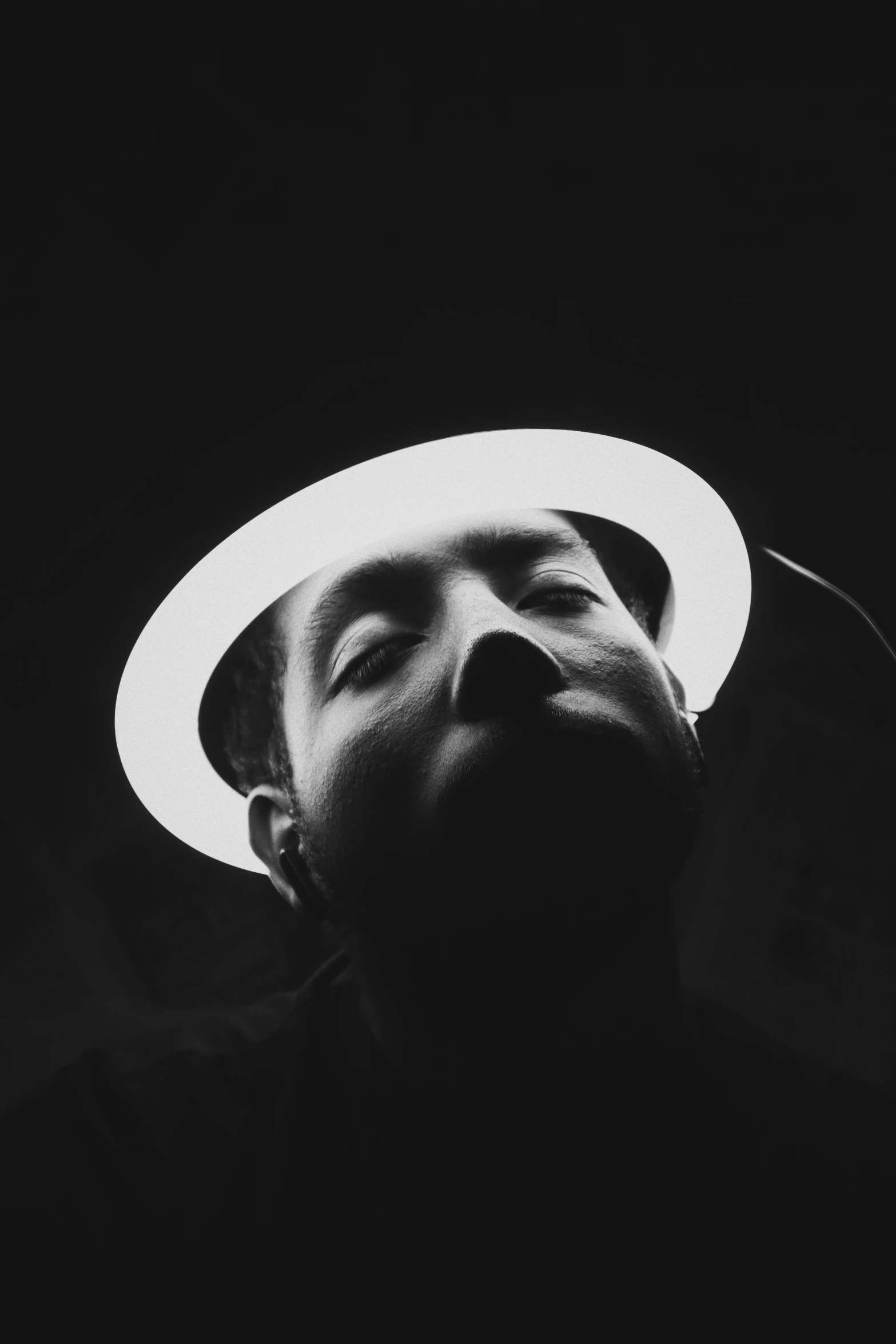 man wearing white hat looking upward, against black background