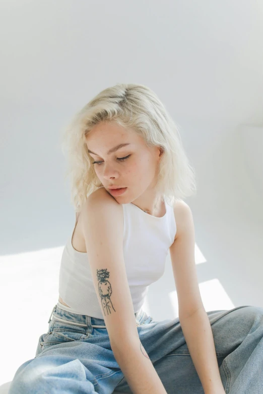 woman with tattoos sitting down wearing white top and jeans