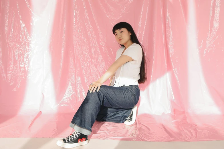 a girl sits against a pink backdrop and poses for the camera