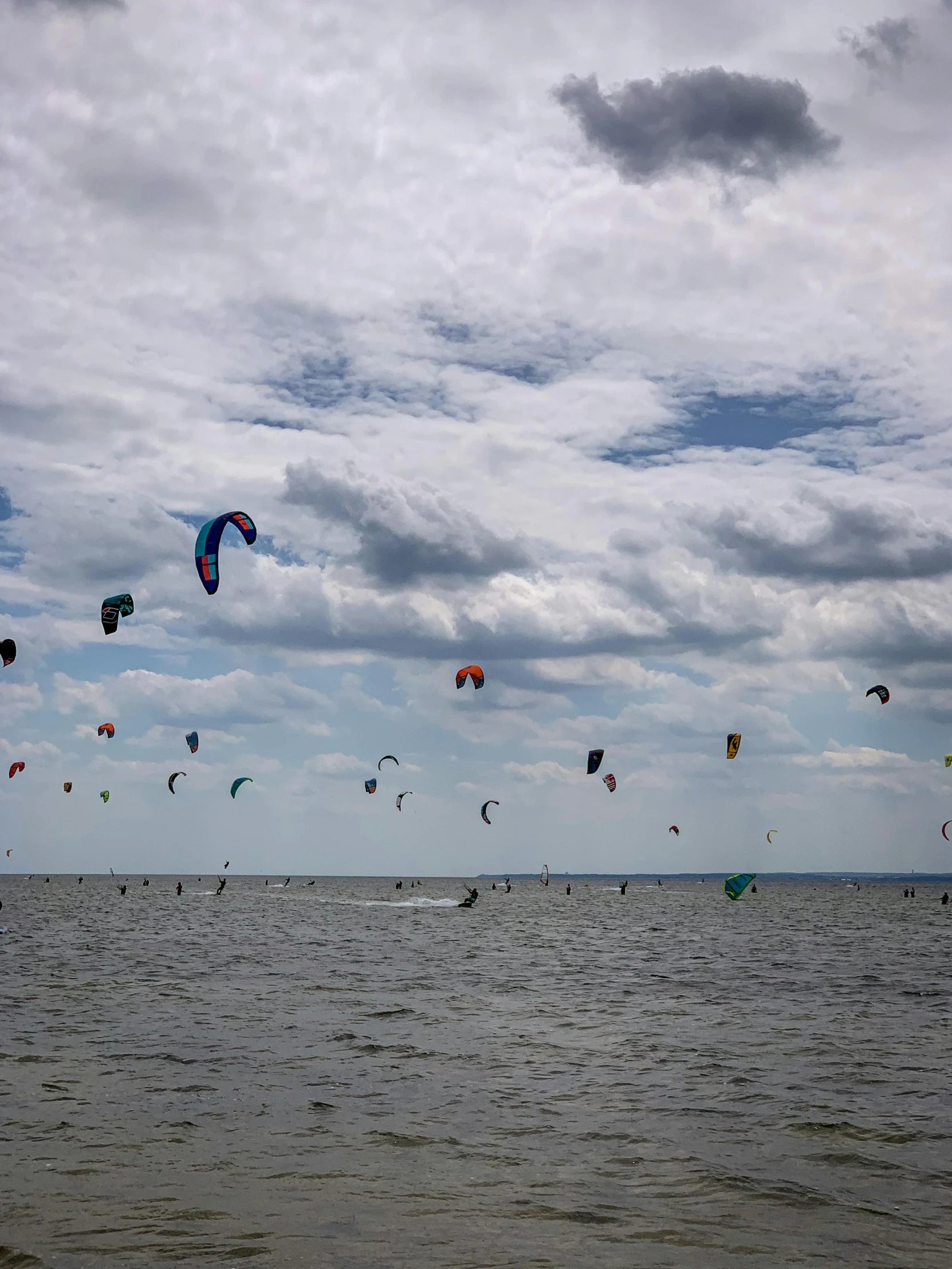 many kites fly over the water beneath a cloudy sky