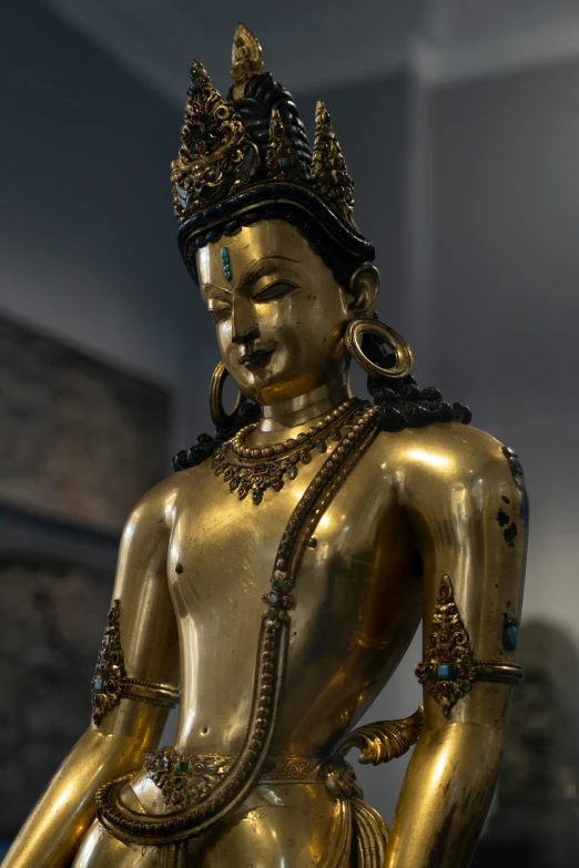 large gold colored statue of woman sitting on top of a wooden table