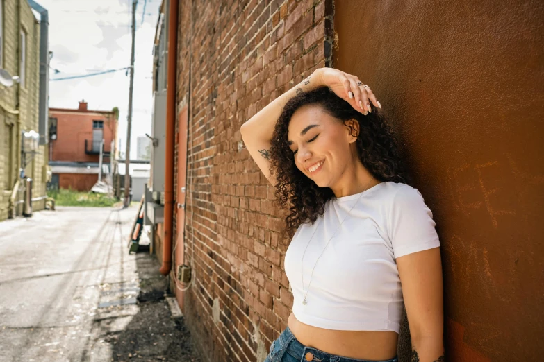 a woman leaning against a brick wall with her hands on her head