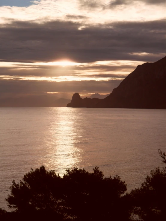 sunset over a mountain in the middle of a body of water