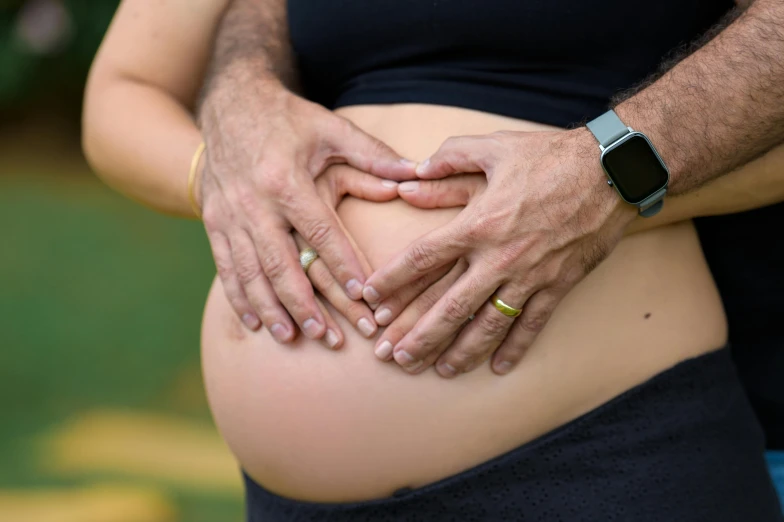 a couple holding hands over the belly of an individual