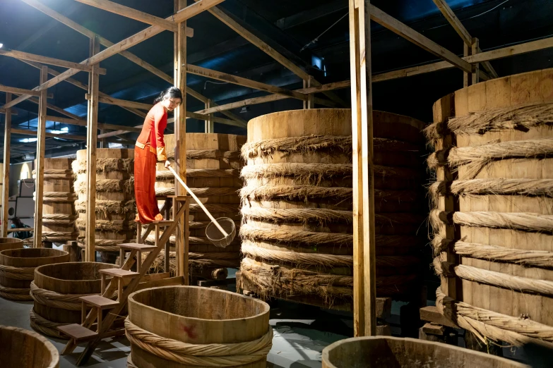person in orange suit cleaning wooden buckets in a factory