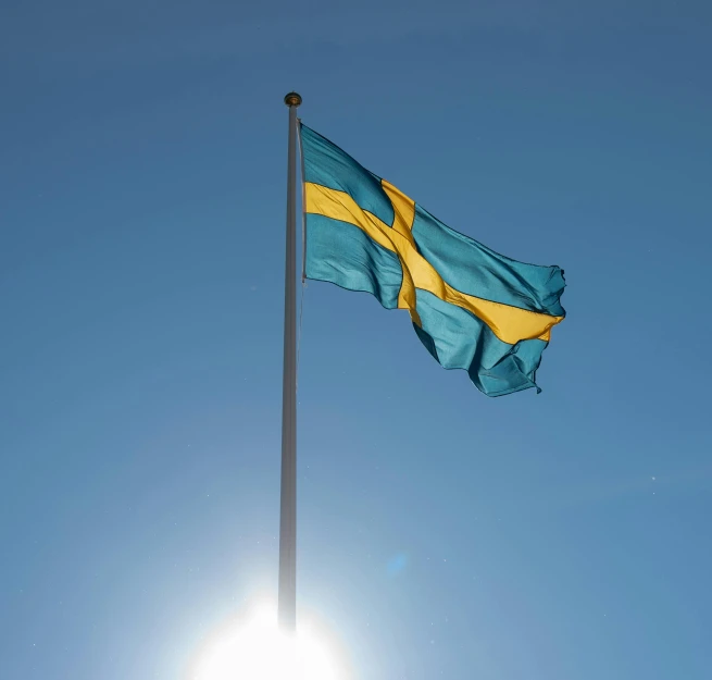 an swedish flag flies in the sun over a clear blue sky