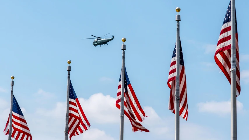 a helicopter flies low over american flags