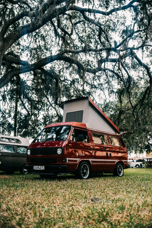 a red van sitting on top of a field next to a tree