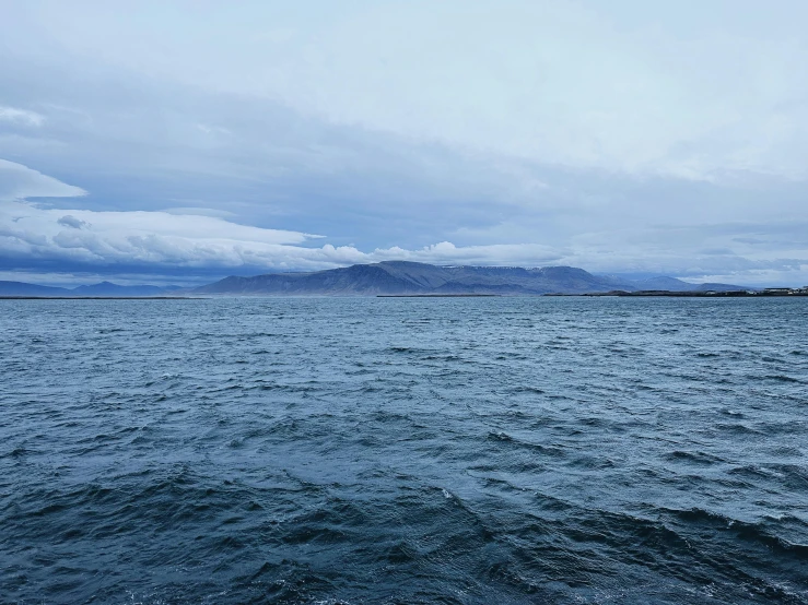 an ocean on a cloudy day with mountain range in the distance