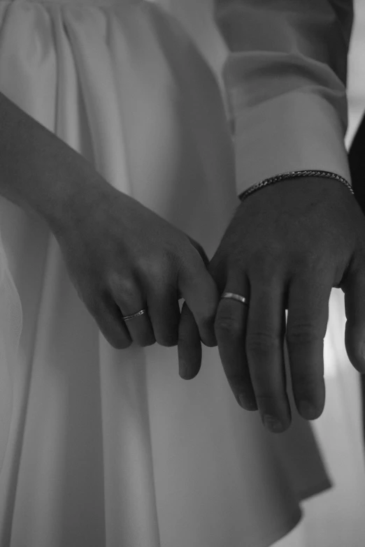 a couple holds hands and wears wedding bands