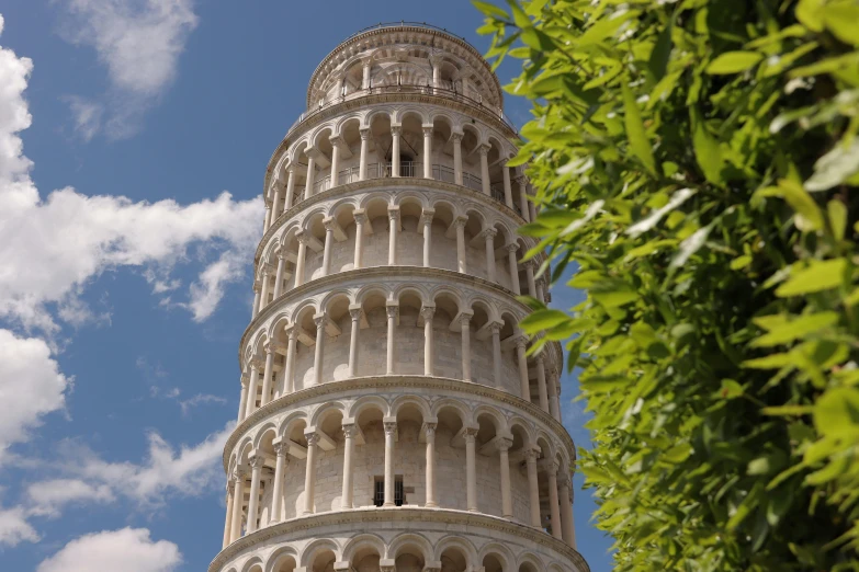 looking up at a tall leaning tower with clocks on the top