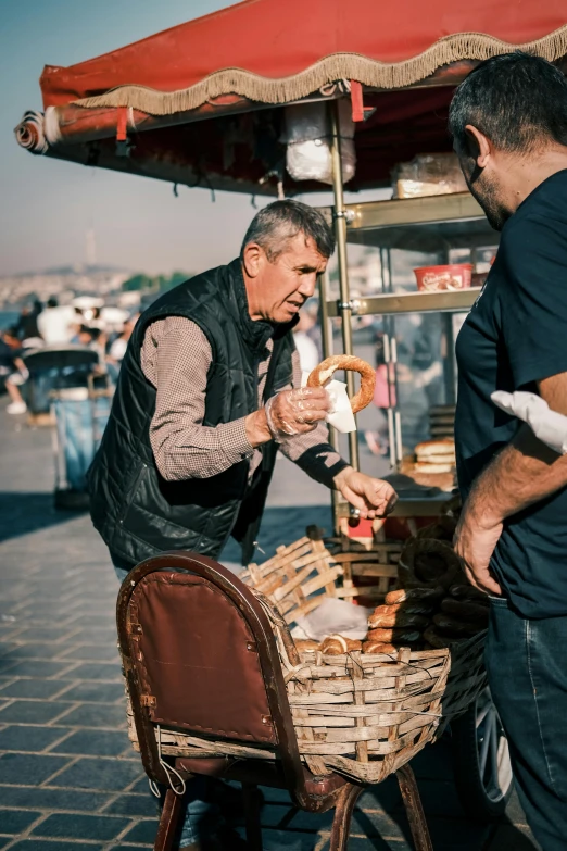 two men on an outdoor food cart with a basket of doughnuts