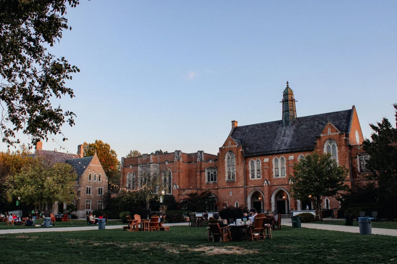 a group of people sitting at tables on grass near a building