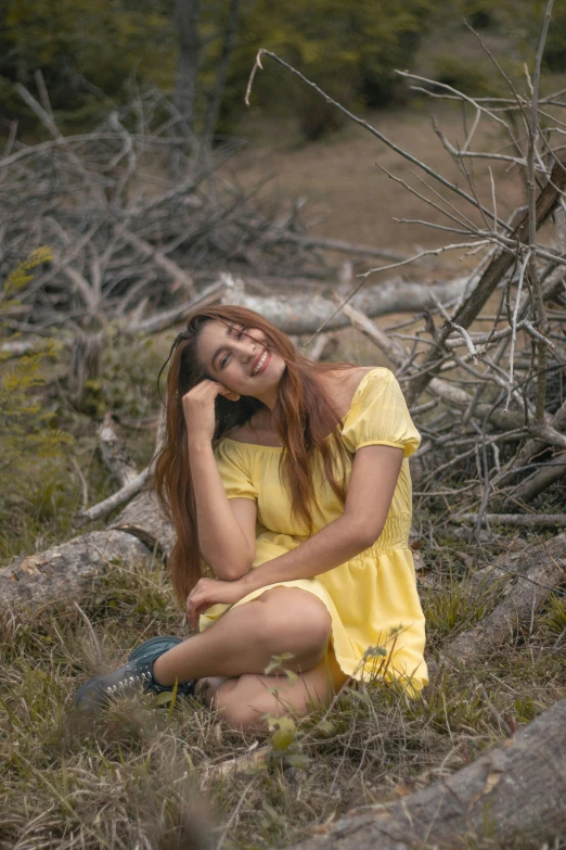 a beautiful young woman in a yellow dress sitting on the ground