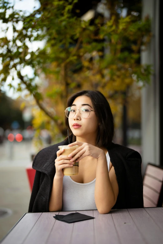 woman at outdoor table drinking coffee, looking up