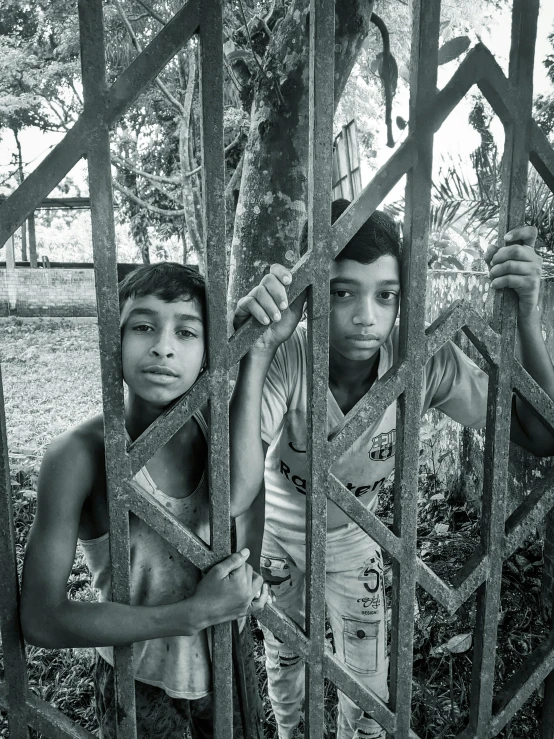 two boys are standing next to each other behind bars