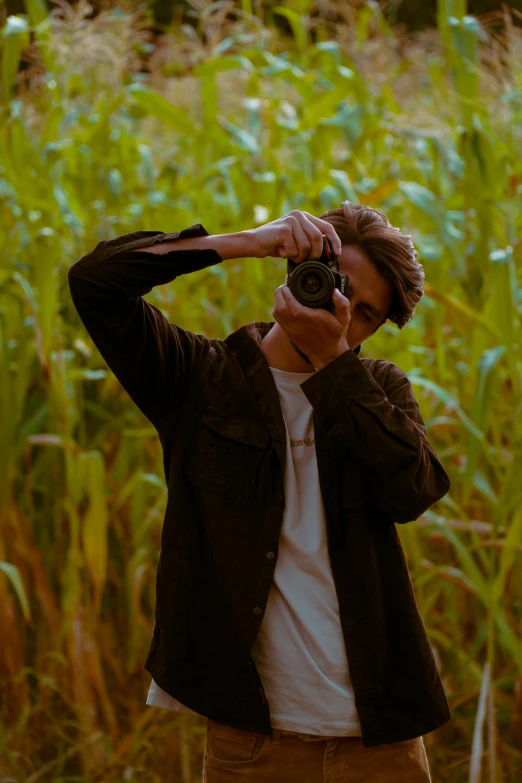 a man taking a pograph with a camera in front of a cornfield