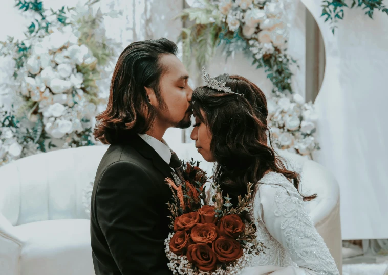 the bride and groom are kissing in front of a large white chair