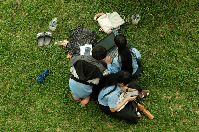 two girls sitting in the grass while looking at their laptops