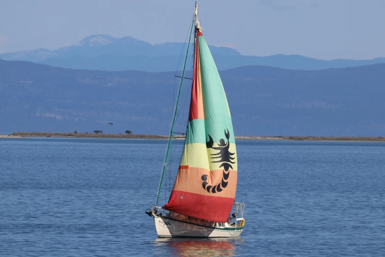 an orange, yellow, blue and green sailboat in the water