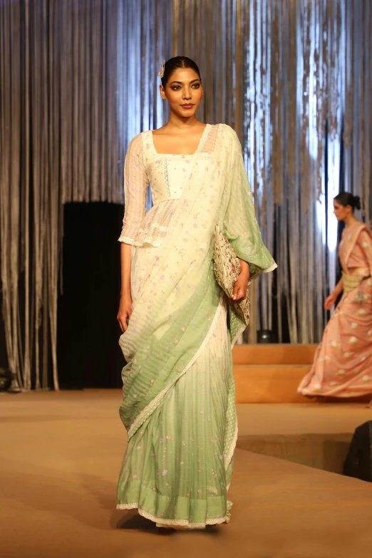 an indian woman wearing a saree walking down the runway