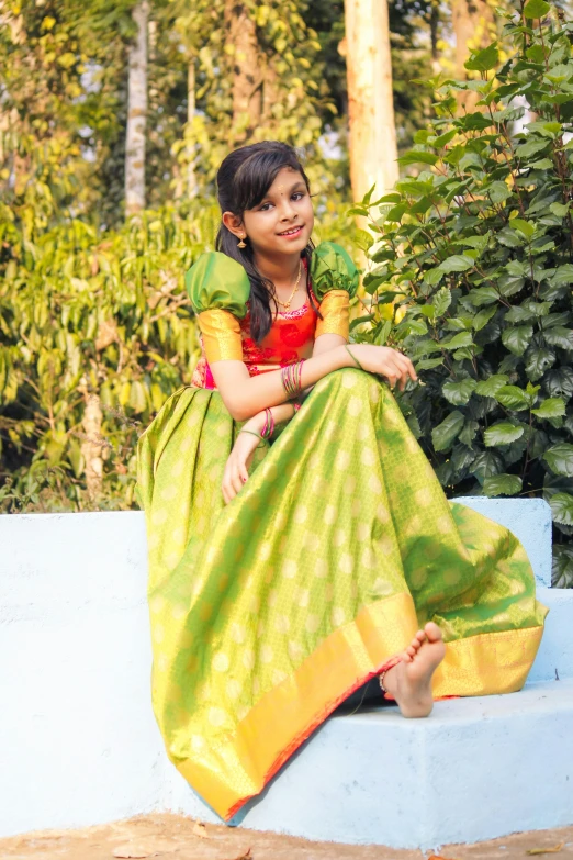 a small child is posing on the edge of a wall wearing a saree