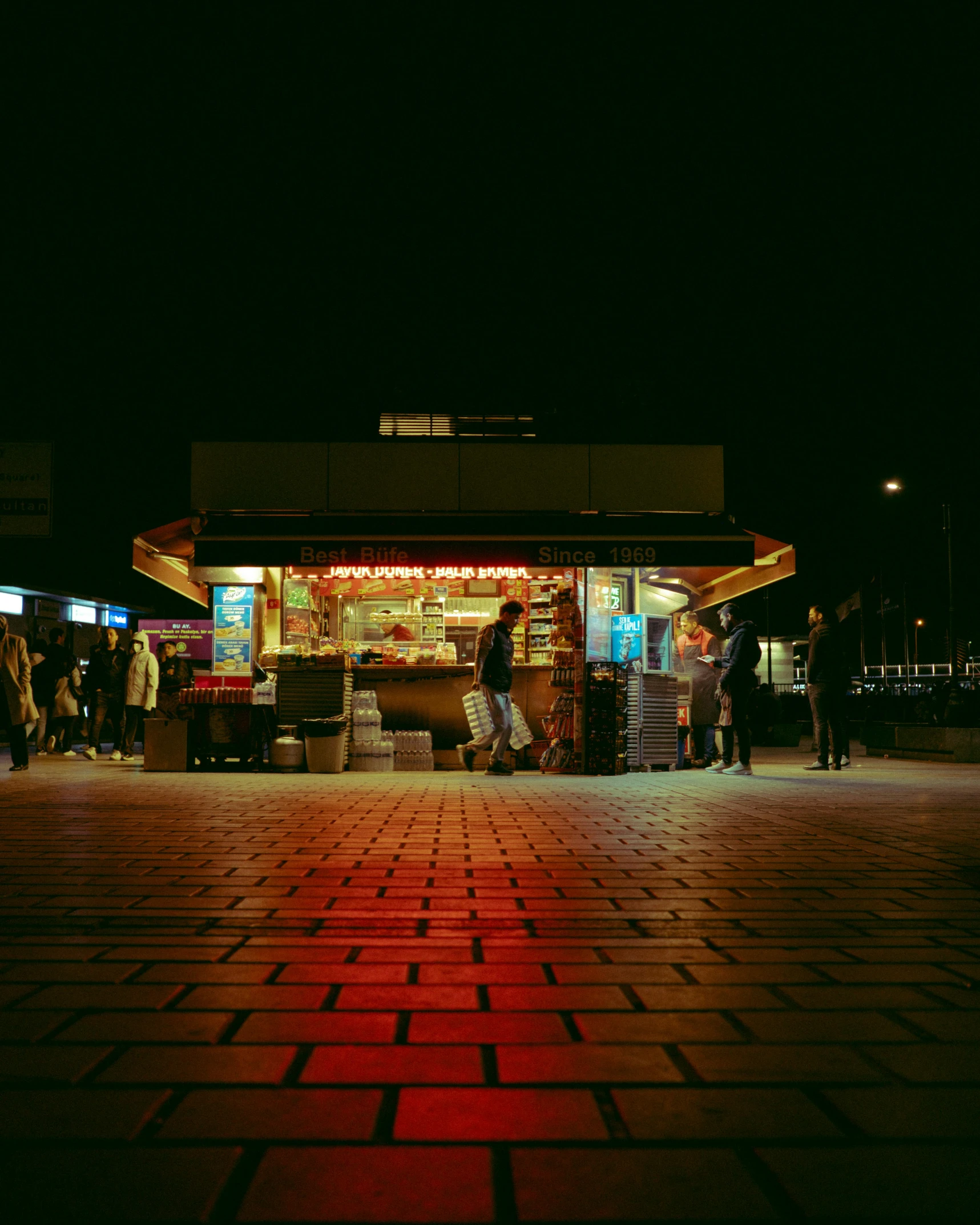 people standing in front of a food stand at night