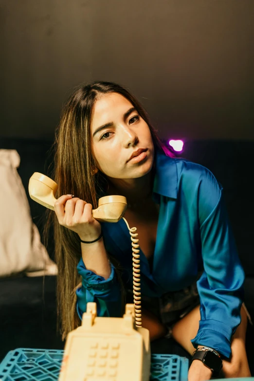 young woman in blue blouse talking on a yellow telephone