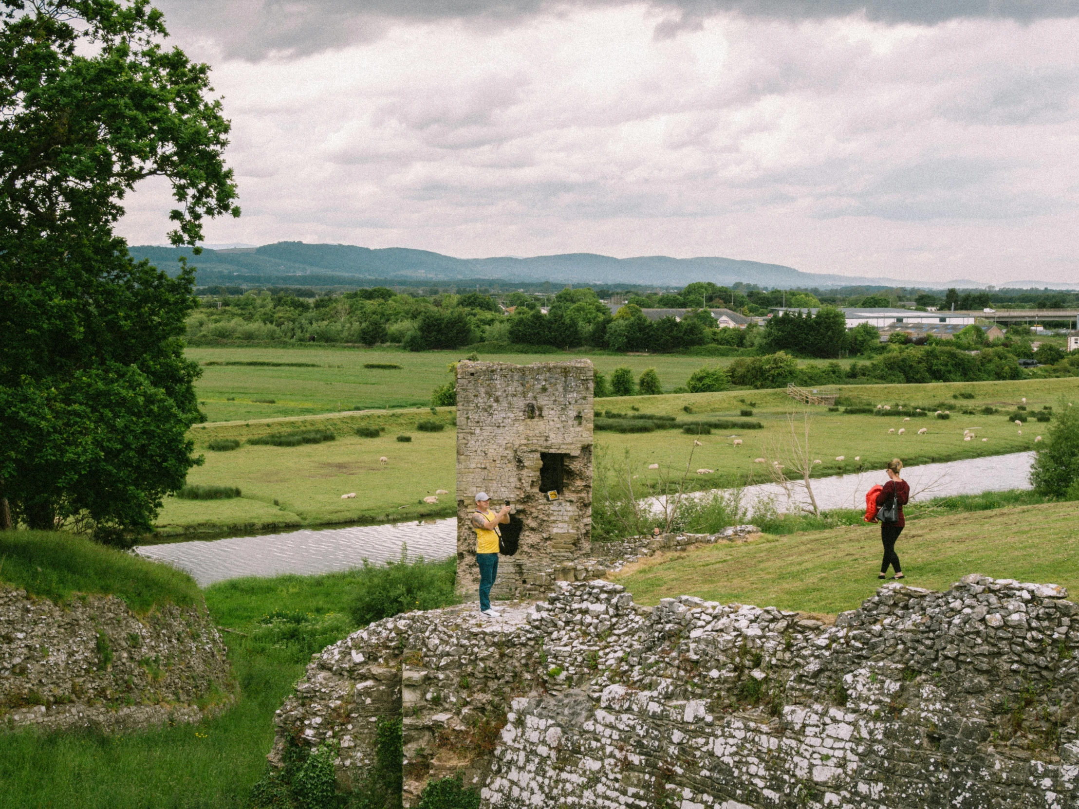 two people standing next to a stone wall overlooking a field
