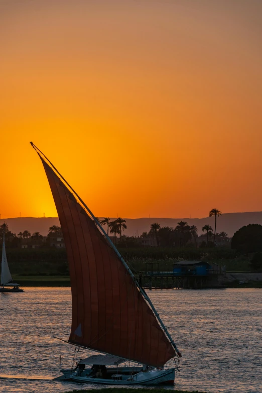 the sun sets over the lake and the sailboats