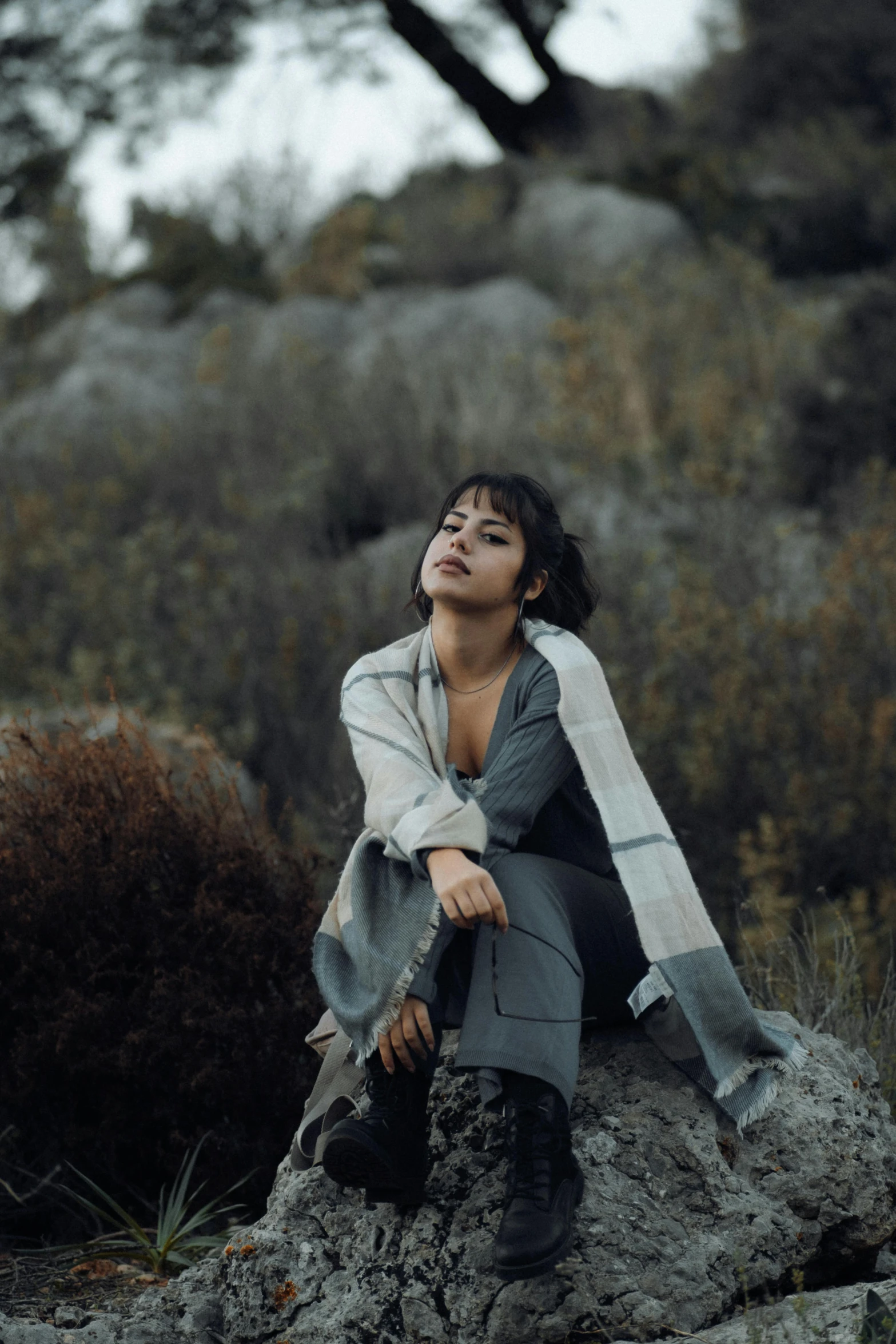 woman sitting on rock gazing at trees on cloudy day