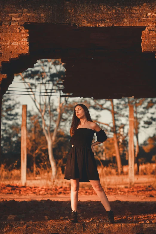 a young woman poses while standing beneath a bridge
