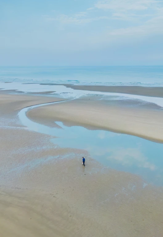 a man is walking along the beach by the water