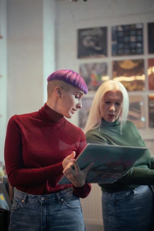 a woman in red shirt standing near another woman with a laptop