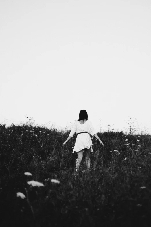 black and white pograph of a girl walking on a field with flowers