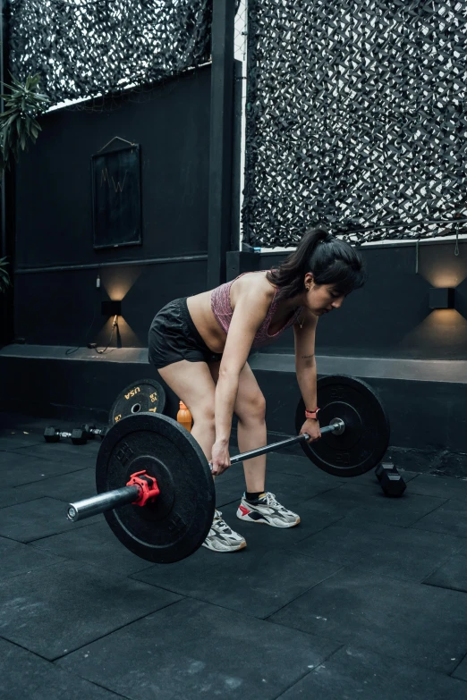 woman with dark skin in shorts and white sneakers lifts a barbell bar