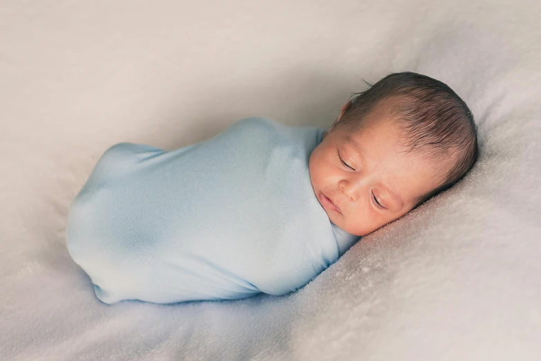 a baby is wrapped in a blue blanket on a white blanket